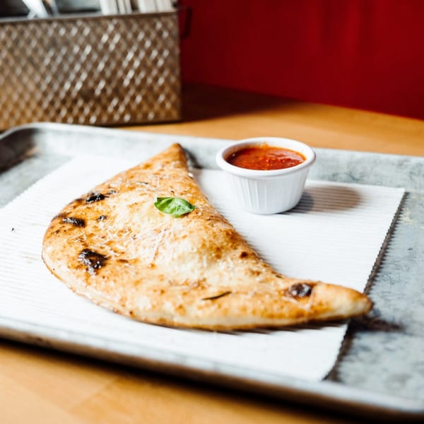 DeSano Pizzeria Napoletana calzone with a side of marinara sauce, garnished with basil.