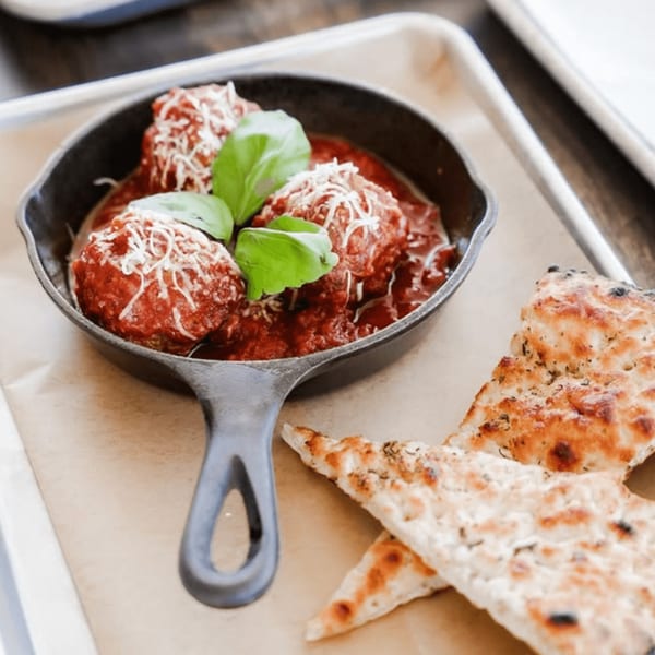 Meatballs in marinara sauce with parmesan cheese and basil, served with flatbread on a tray.