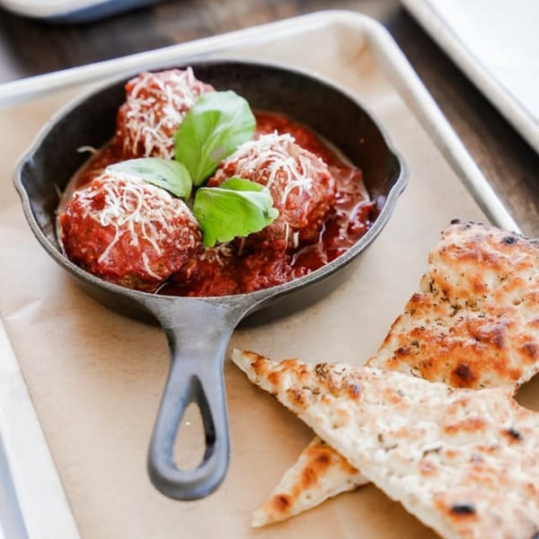 Meatballs in red sauce with parmesan and basil in a cast iron pan, served with flatbread.